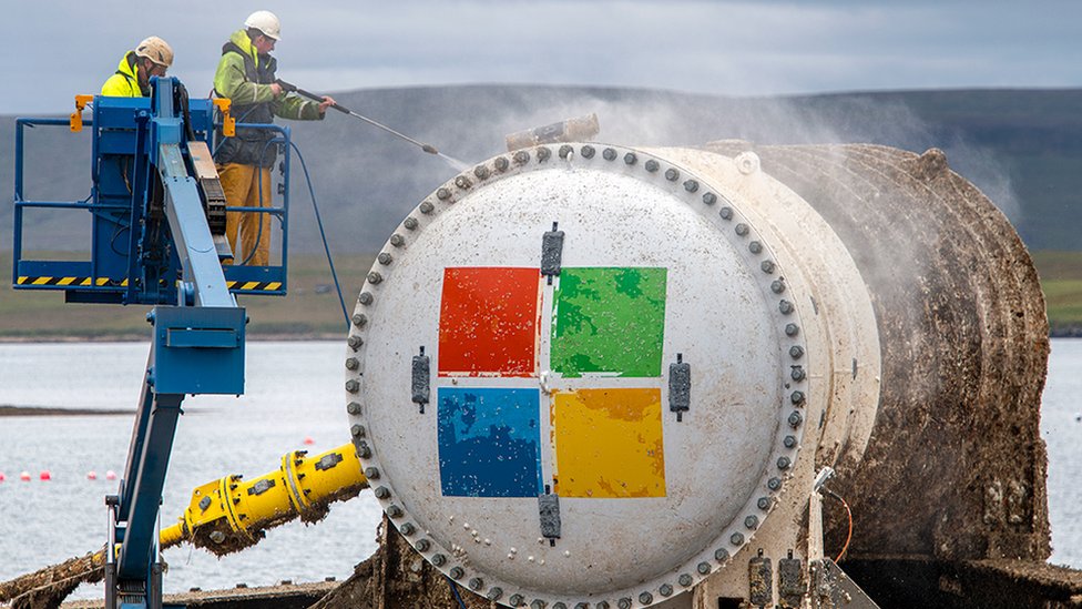 Two men power-wash the exterior of the Microsoft data centre capsule