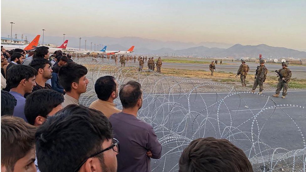阿富汗人擠在機場附近的鐵絲網後面注釋著前面的美軍士兵