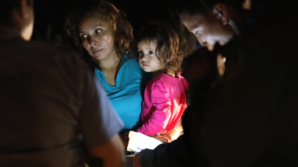 Madre Salvadoreña con su hija de dos años en brazos mientras la guardia fronteriza de EE.UU. inspecciona sus documentos