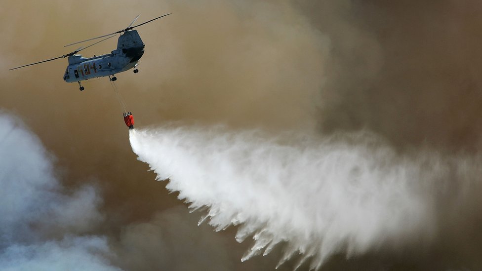 Helicóptero sobrevoa um incêndio florestal depositando água