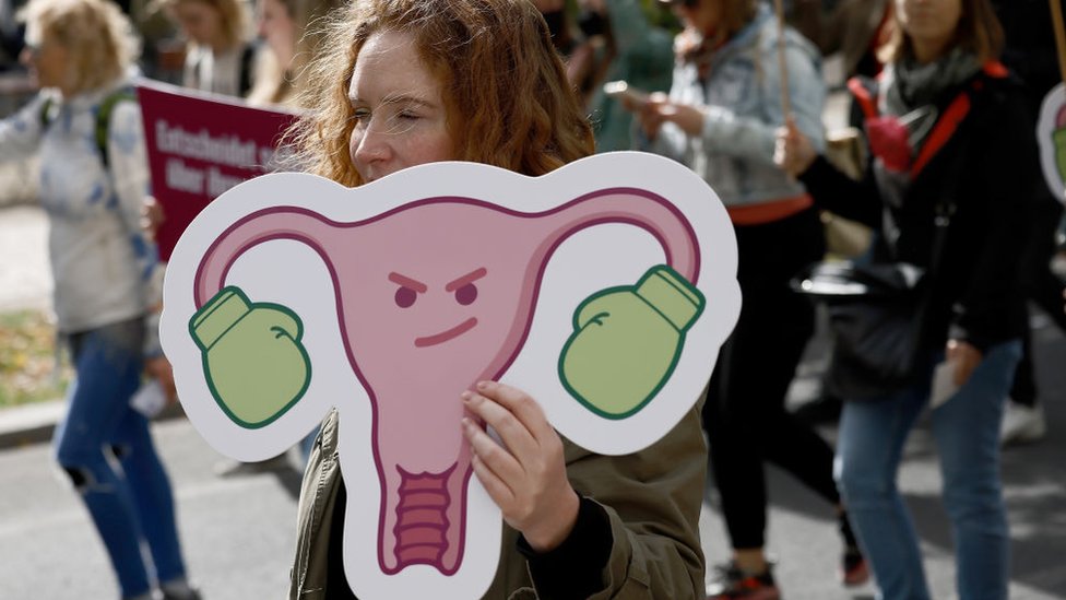 Mujer en una manifestación con una pancarta en la que se ve a un útero que lleva sendos guantes de boxeo en las trompas de Falopio.