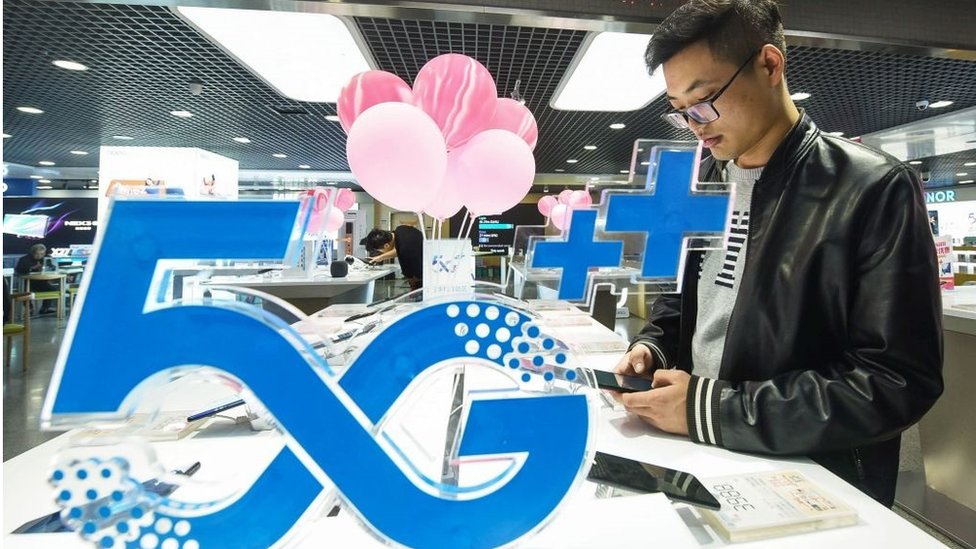 Покупатель смотрит на мобильный телефон рядом с логотипом 5G в магазине в Ханчжоу в восточной китайской провинции Чжэцзян 31 октября 2019 г.