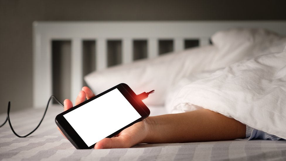 Persona en la cama agarrando un celular conectado.