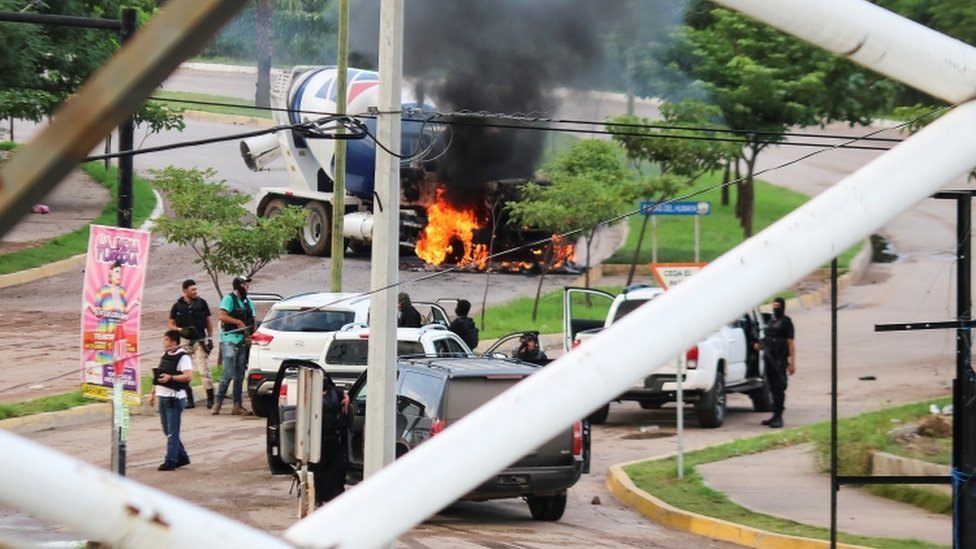 Боевики картеля видны возле горящего грузовика во время столкновений с федеральными силами