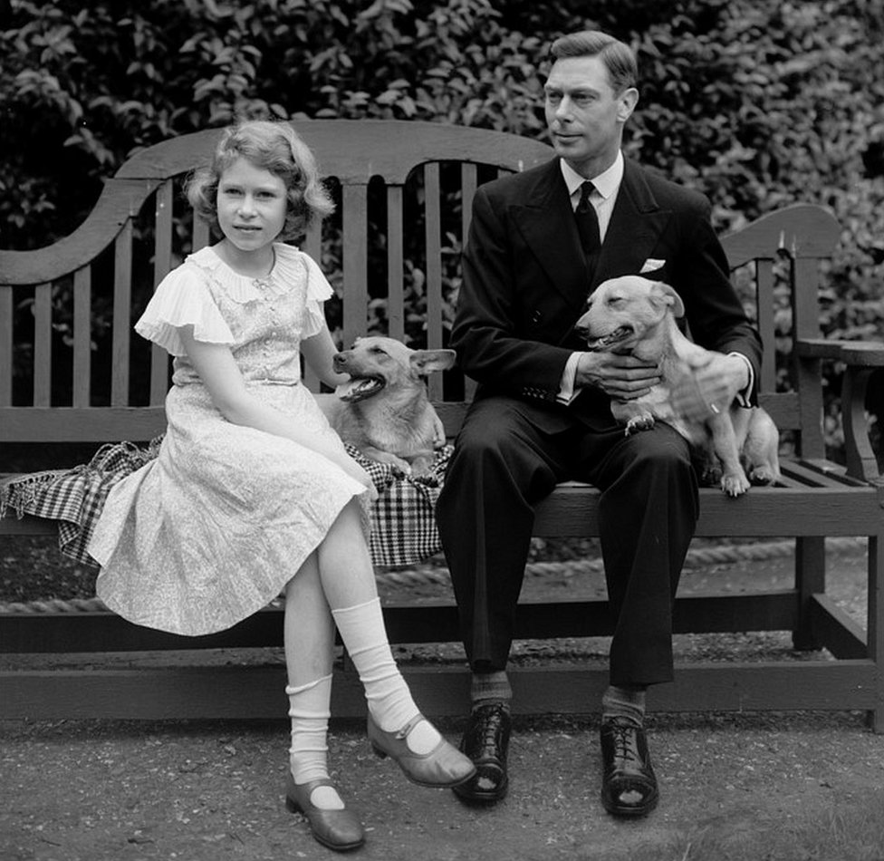 July 1936: George, Duke of York and Princess Elizabeth sitting on a bench with their corgi dogs in the grounds of their London home, 145 Piccadilly.