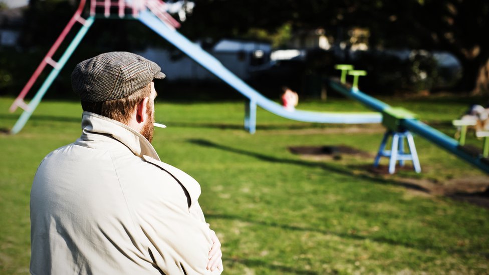 Un hombre de espaldas observando niños en un parque.
