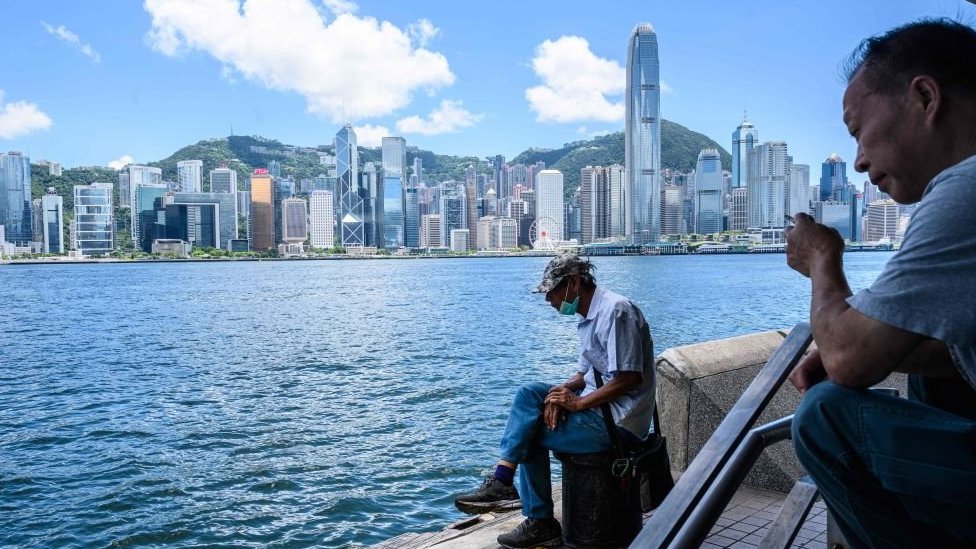 Мужчина сидит на стороне Коулун гавани Виктория, которая обращена к горизонту острова Гонконг.