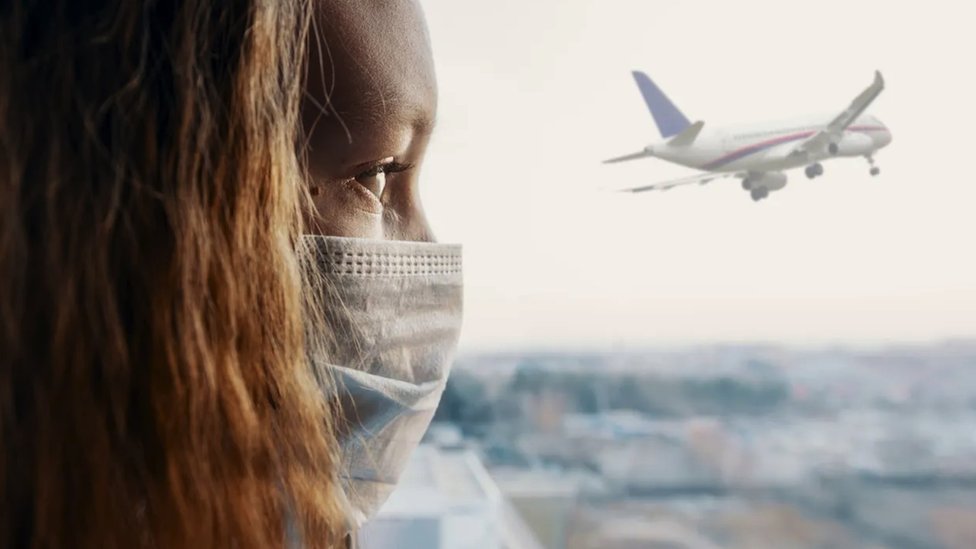 Woman in mask looks at aeroplane in the sky