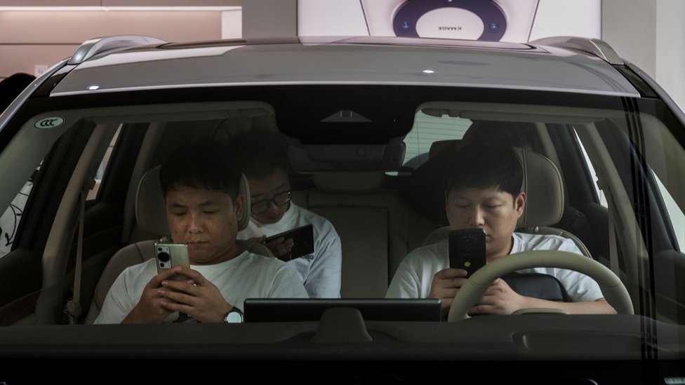 Customers look at their phones as they sit in a Huawei electric car watching a a livestream of an event to launch new products, at a Huawei flagship store on September 25, 2023 in Beijing, China