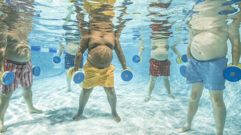 Corpos de homens fazendo hidroginástica vistos debaixo d'água