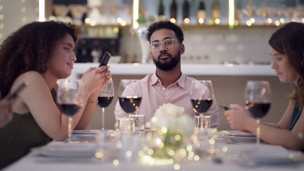 Mesa de jantar com pessoas entediadas e digitando no celular