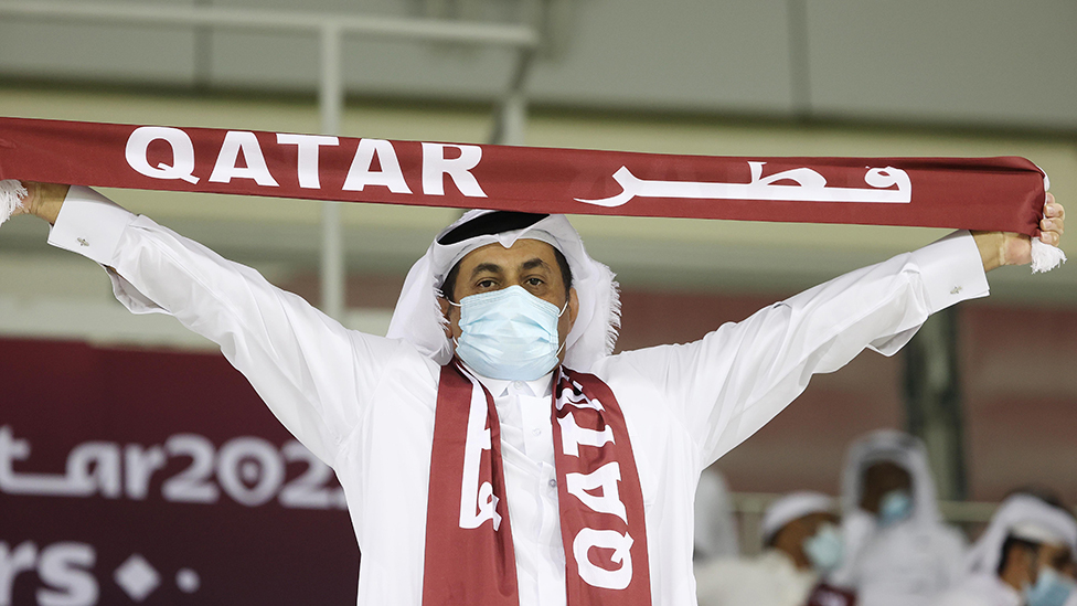 man in mask holds Qatar football scarf