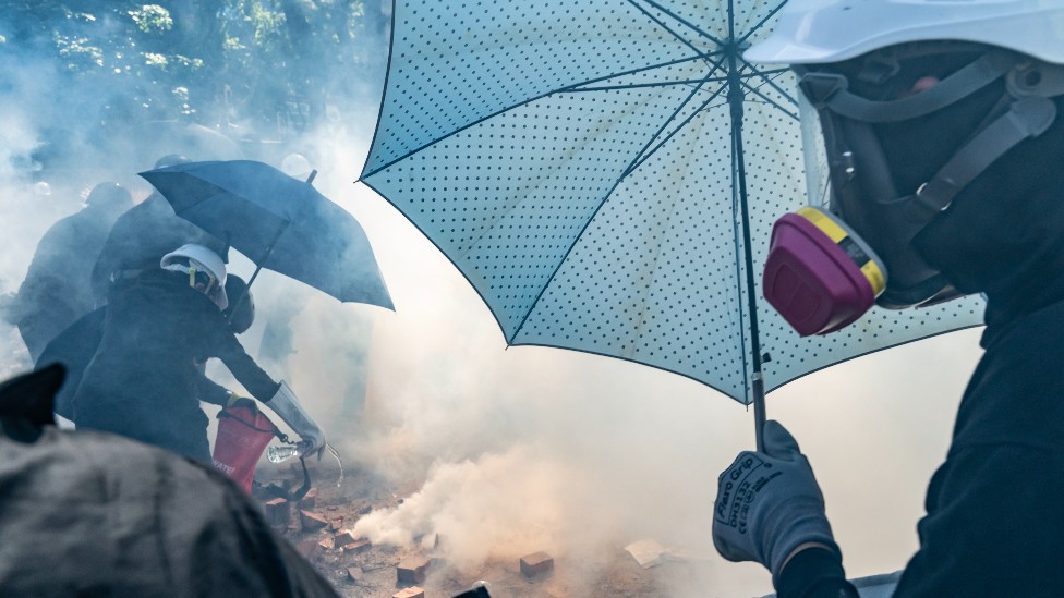 Manifestantes con paraguas y mascarillas.