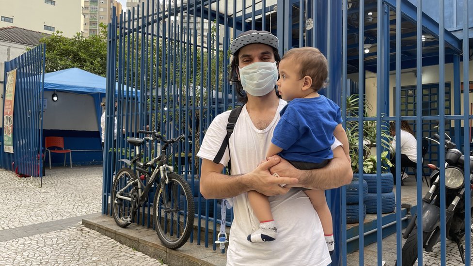 Renan Bidutti de máscara com o filho no colo, em frente a posto de saúde
