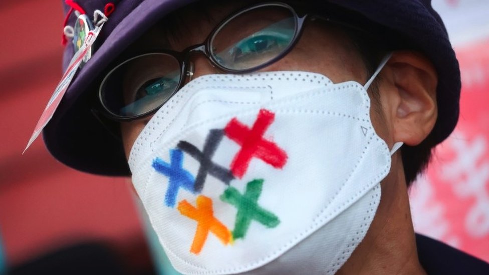 A man wears a facemask with Olympic colours on it protesting against the Games