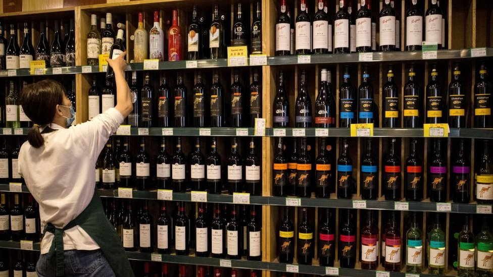 Работник магазина берет бутылку из секции австралийских вин в магазине бутылок в Пекине