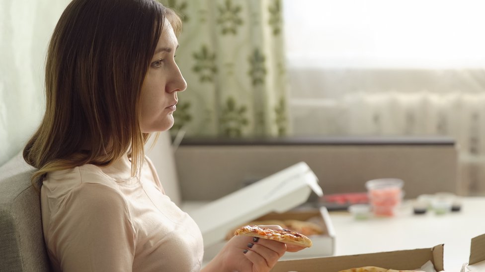 Mujer triste comiendo pizza sola en un sofá