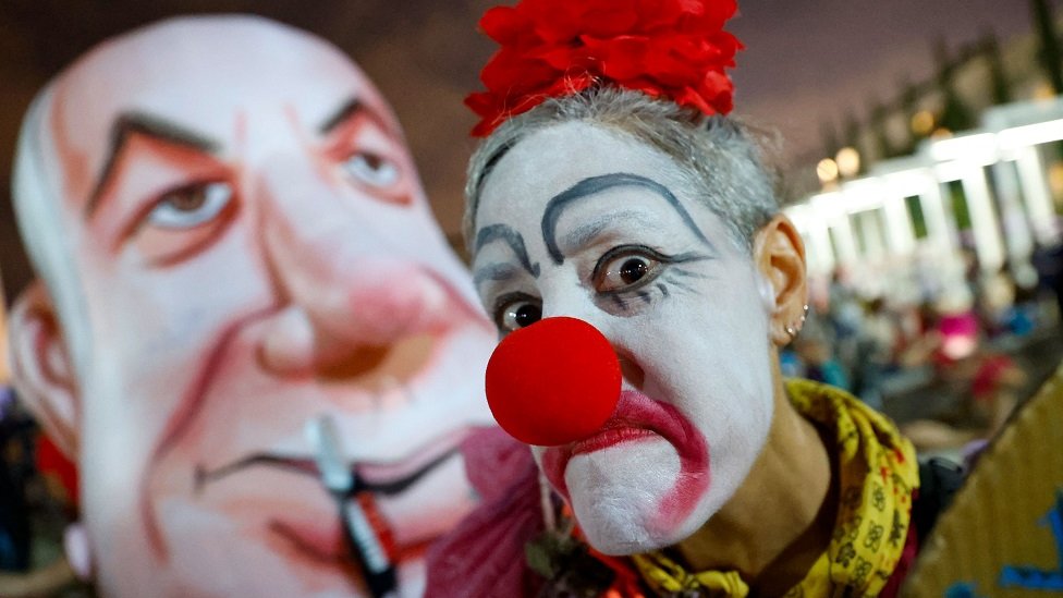 An Israeli woman wearing a clown outfit mocks Prime Minister Benjamin Netanyahu as she takes part in a demonstration against the government and an imminent and unprecedented second nationwide lockdown to tackle a spike in coronavirus, in Tel Aviv, on 17 September 2020.