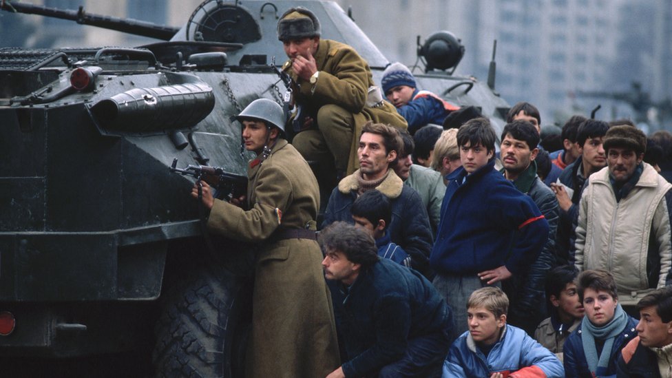 Romanian soldiers and civilians take cover behind a tank in Bucharest's Palace Square in December 1989
