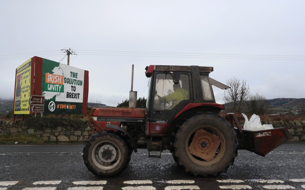 Фермер на тракторе проезжает акцию протеста против Брексита мимо знаков возле ирландской границы