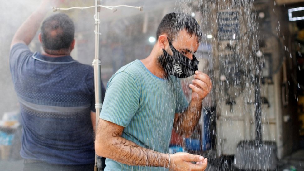 A man wearing a face mask stands under an outside shower in Baghdad on 28 July