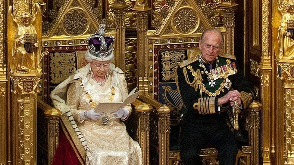 La reina de Inglaterra ofrece su tradicional discurso desde un trono de oro. La reina Isabel II de Inglaterra leyendo un discurso desde un trono de oro