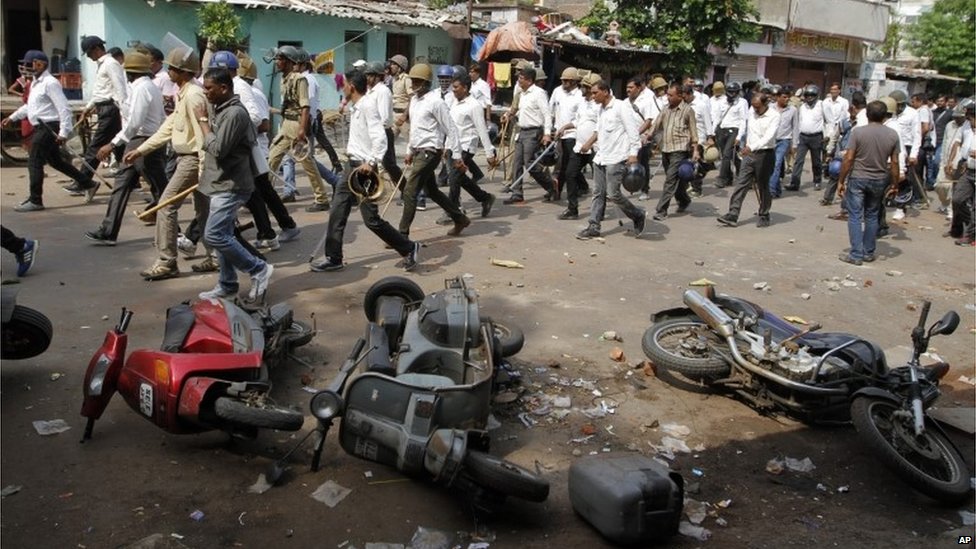 Индийские полицейские в штатском проходят мимо автомобилей, поврежденных во время столкновения двух групп в Ахмадабаде, Индия, во вторник, 25 августа 2015 г.