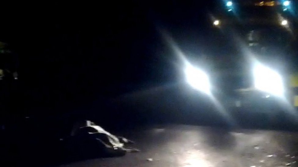 На кадре из любительского видео с телефона, снятого камерой, видно укрытое тело в Уэйбридже, рядом стоит полицейская машина, 10 ноября