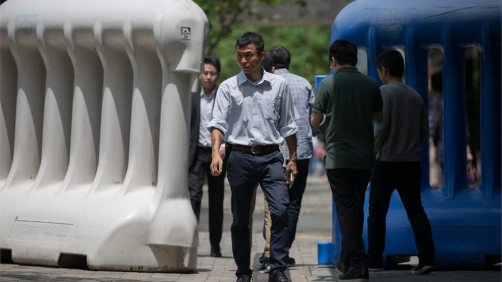 Пешеходы проходят между водными преградами, которые используются для оцепления зоны безопасности, где будет проживать глава китайского государства Чжан Дэцзян, и выступят с речью во время своего трехдневного визита в Гонконг, Китай, 16 мая 2016 года.