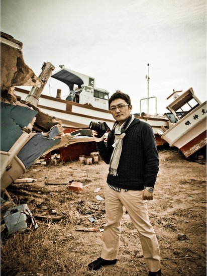 Repórter com câmera nas mãos em meio aos escombros deixados pelo tsunami