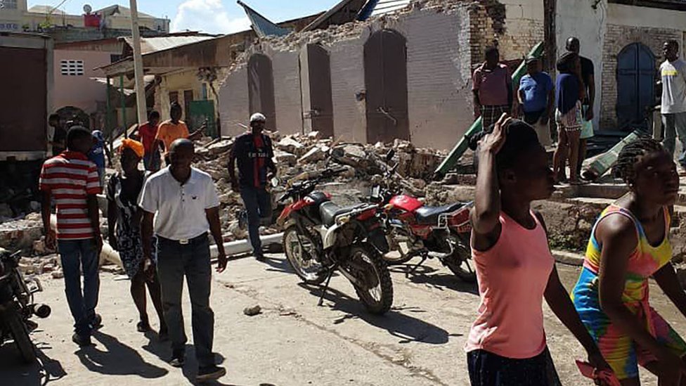 Grupo de personas pasa delante de una casa en ruinas en Haití