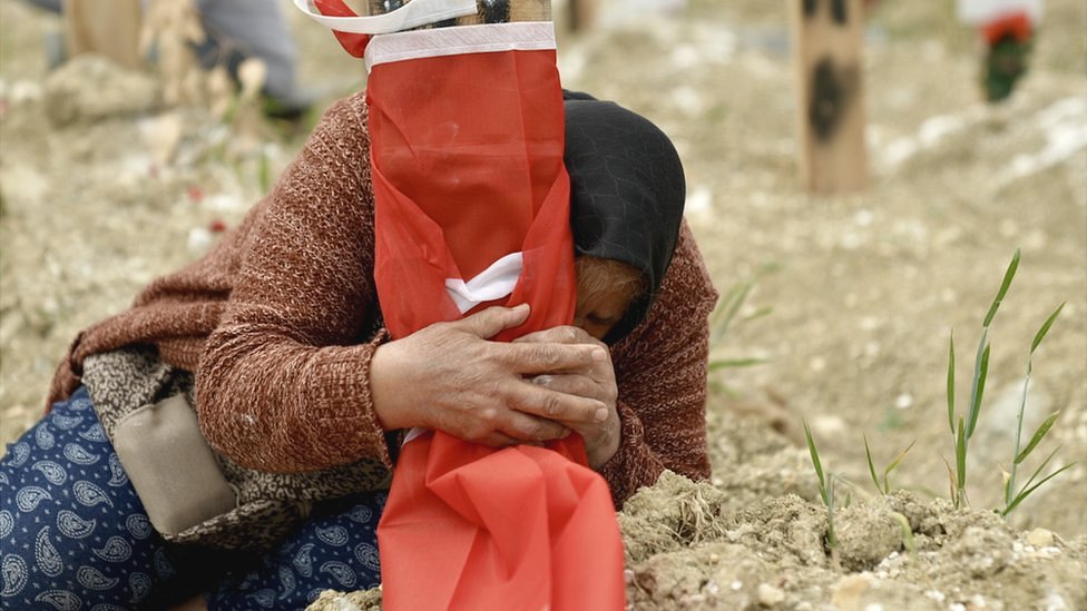 Fethiye Keklik clutching the makeshift grave marker where her son, who died in the quake, is buried