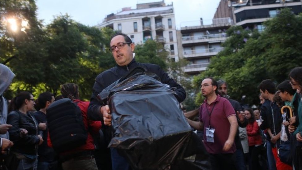 Este hombre lleva una de las cajas donde se prevé que se introduzcan los votos de quienes asistan a la jornada electoral en la Escola Industrial de Barcelona, mientras decenas de personas se reúnen afuera para impedir que la policía entre. Un hombre con una caja