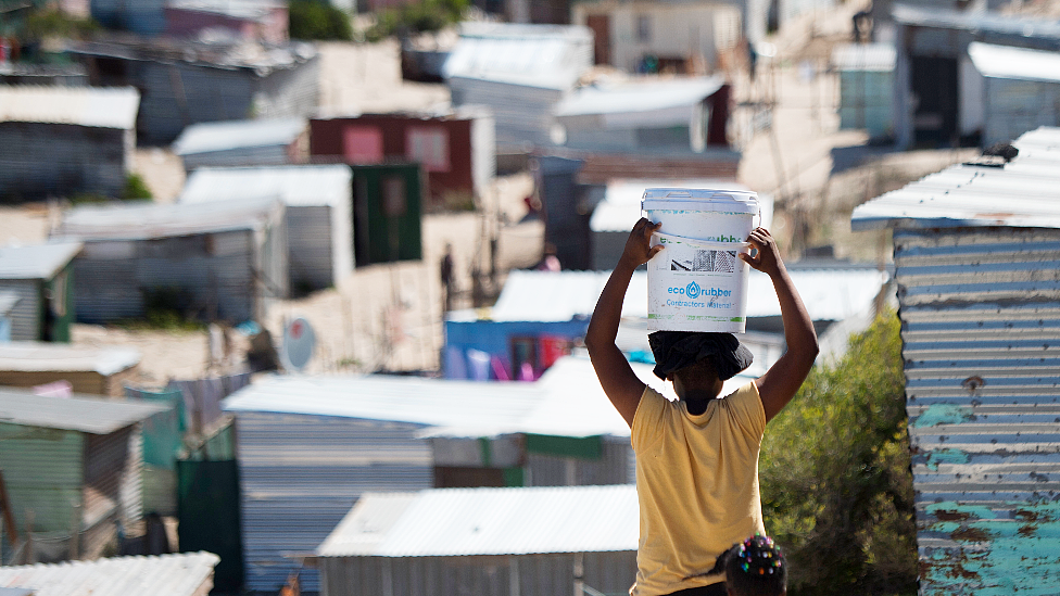 Una mujer llevando un balde de agua a un asentamiento informal en Khayelitsha, cerca de Ciudad del Cabo, Sudáfrica.