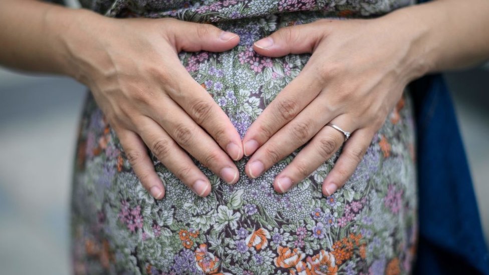Expectant mother Jamie Chui, 33, rests her hands upon her baby bump, while living in lockdown in Hong Kong