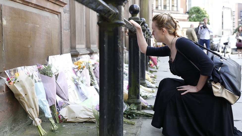 Женщина молится, глядя на цветочные дары, оставленные за пределами церкви Святой Анны в Манчестере после взрыва бомбы на Манчестер-Арене