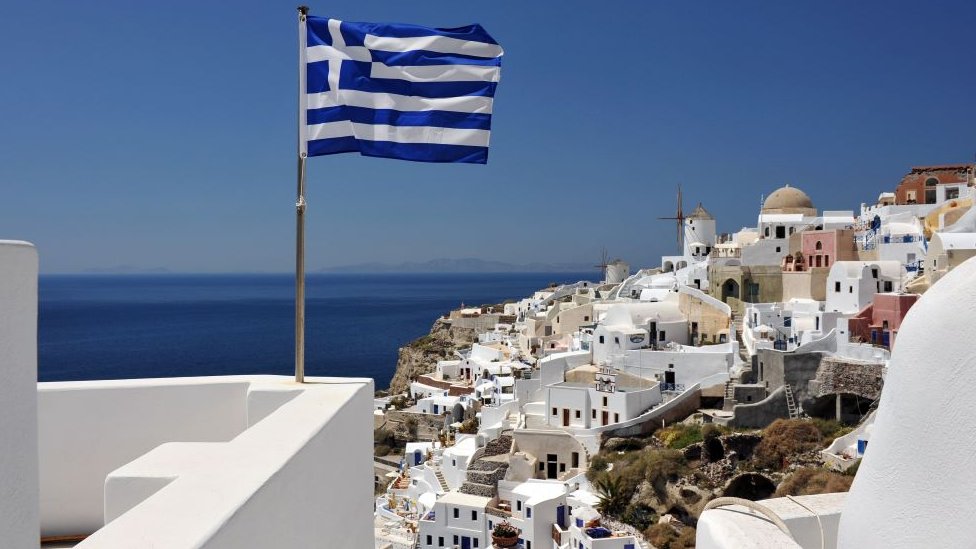 Zastava Grčke se vijori iznad belih kuća na ostrvu Santorini