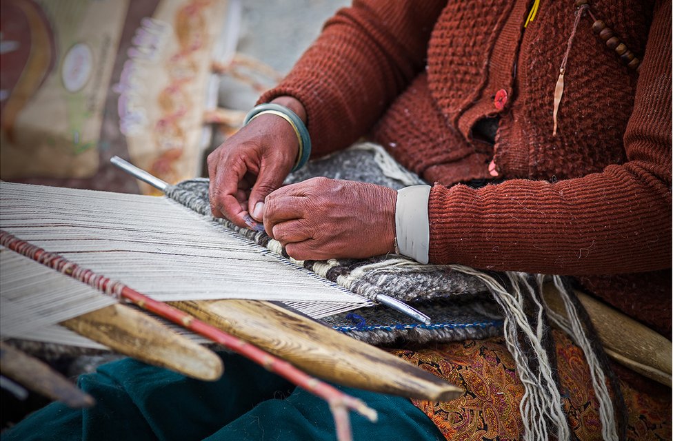 Женщина плетет нитки на ткацком станке у себя на коленях