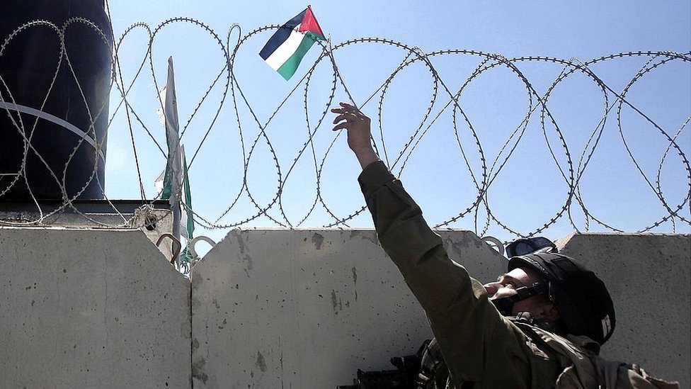 Un soldao israelí retira una bandera palestina del tope del muro en Cisjordania. Soldado israelí retira una bandera palestina del muro en Cisjordania