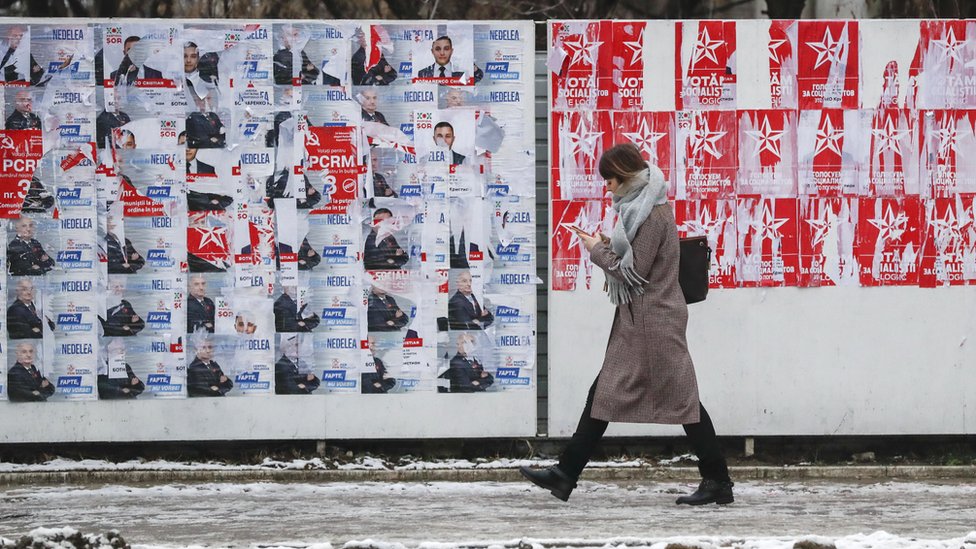 Žena prolazi pored zida na kojem se vide posteri suparničkih političkih kandidata u Moldaviji