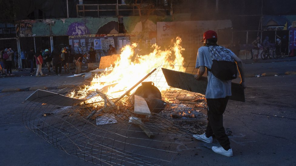 Демонстрант строит горящую баррикаду во время национальной забастовки и всеобщей демонстрации, созванной различными профсоюзами рабочих 12 ноября 2019 года в Сантьяго, Чили.