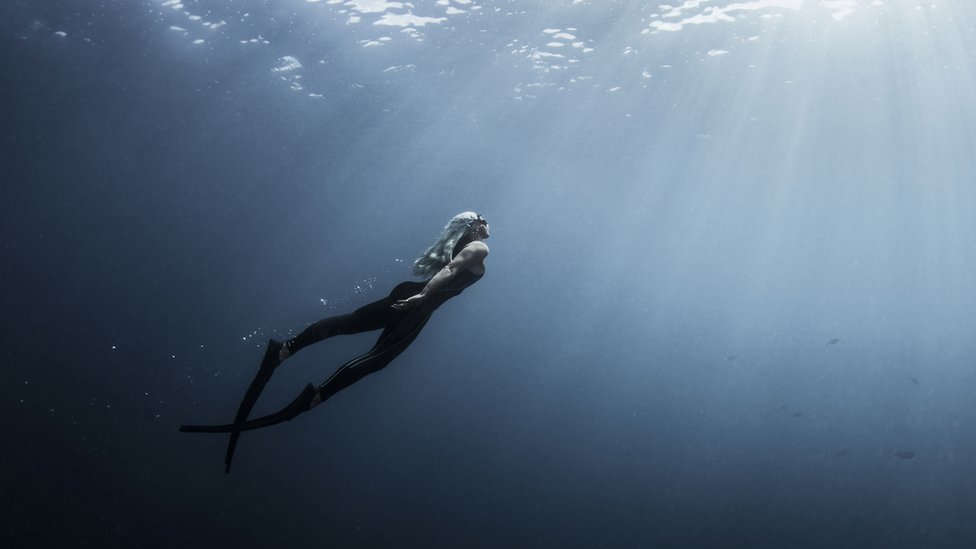 Underwater view of female free diver moving up towards sun rays, New Providence, Bahamas - stock photo