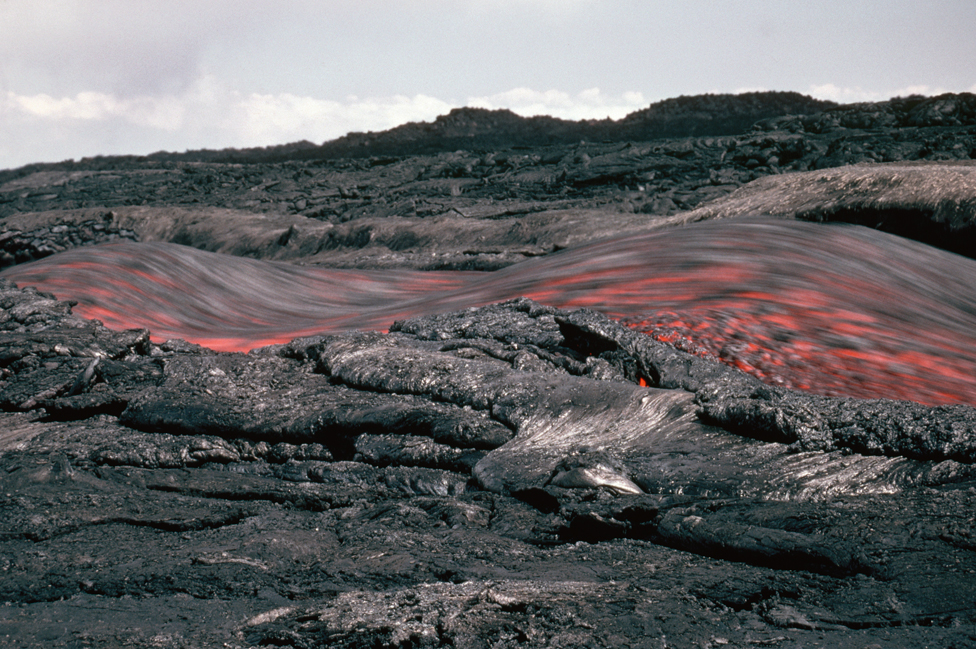 A channel of fast-flowing lava moves through a cooled section of a lava flow. Hawaii.