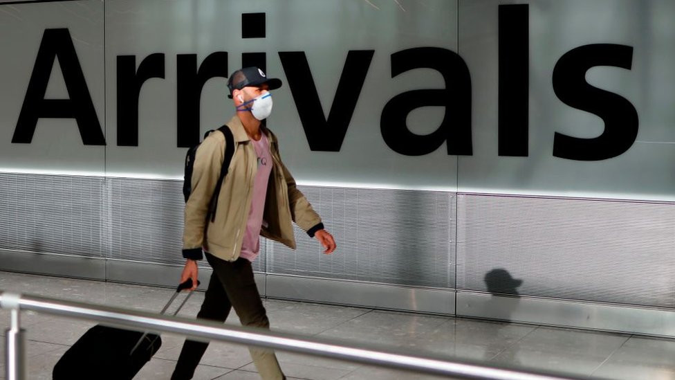 Мужчина в маске тащит свой чемодан через аэропорт