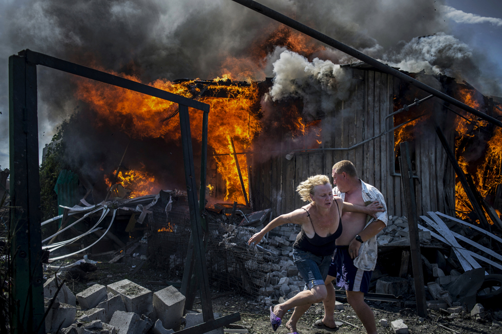 Пара спасается от пожара в доме, разрушенном в результате авиаудара в станице Луганская, Украина.