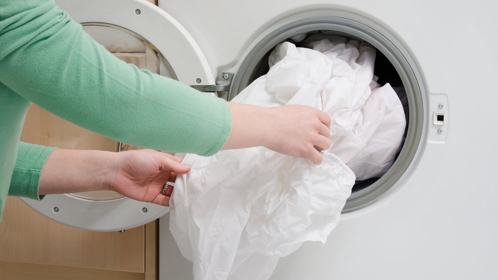Las manos de una mujer llenando la lavadora con ropa de cama.