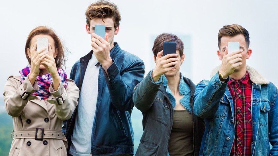 Cuatro personas jóvenes sostienen teléfonos inteligentes frente a sus caras
