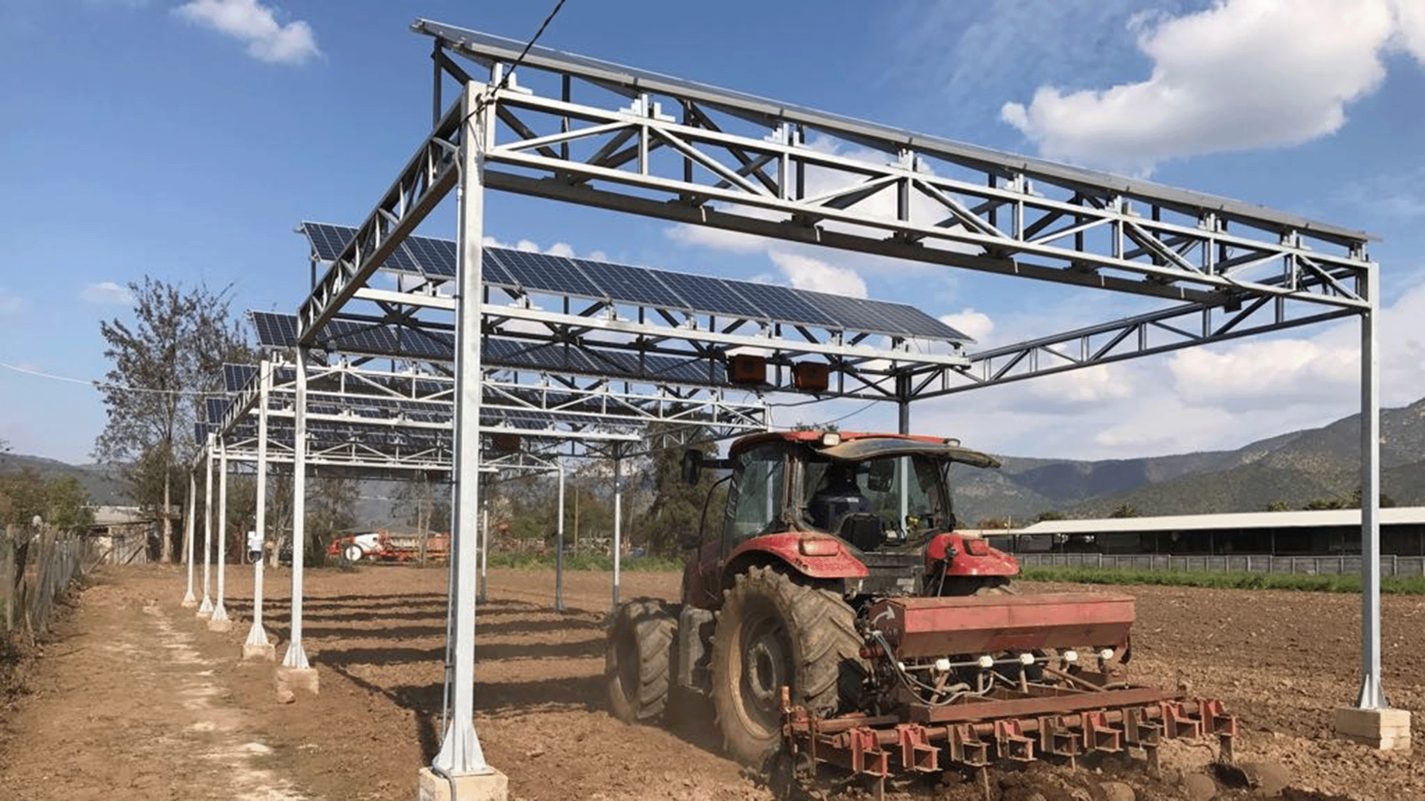 Farm tractor passing below elevated solar panels in an agricultural field in Chile