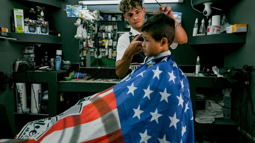 Niño cortándose el pelo en Honduras cubierto con la bandera estadounidense.