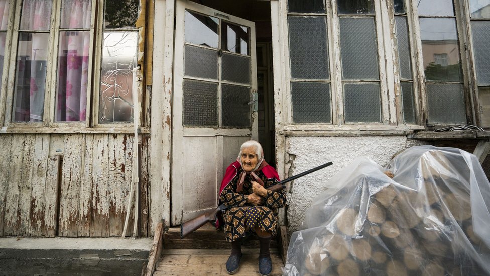 Seorang perempuan lansia berjaga di depan rumah di kota Stepanakert dengan senjata di tangannya